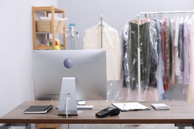 Photo of Dry-cleaning service. Computer monitor, payment terminal and stationery at workplace indoors, space for text