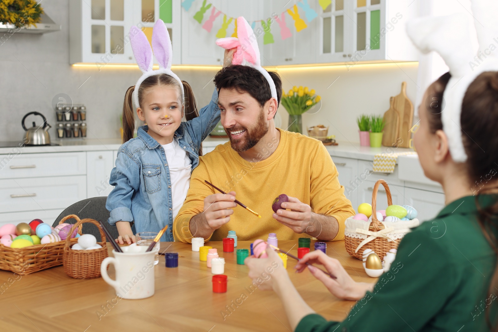 Photo of Happy family having fun while painting Easter eggs at table in kitchen