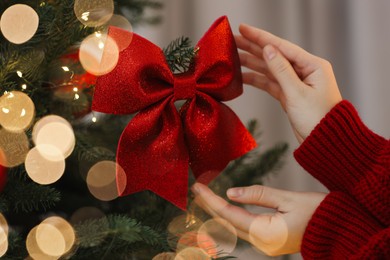 Photo of Woman decorating Christmas tree with red bow on light background, closeup