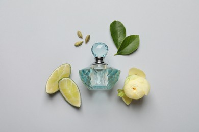 Flat lay composition with bottle of perfume, lime and  flower on light grey background