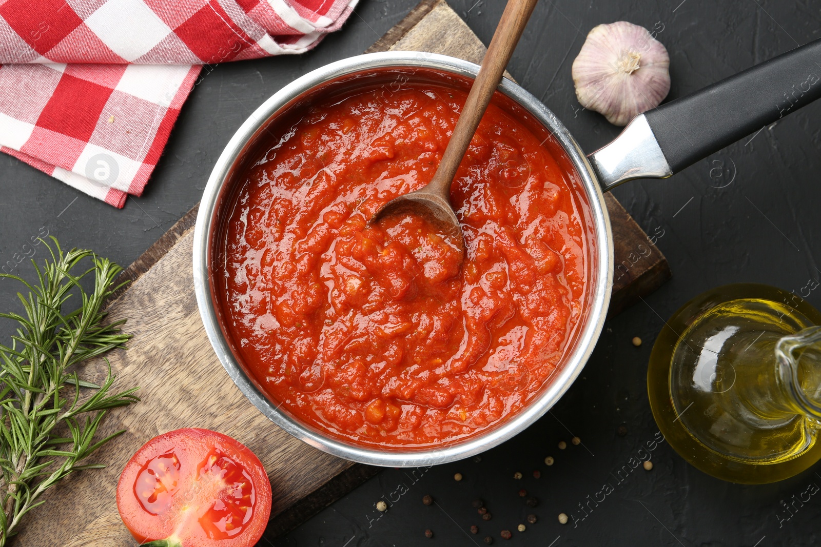 Photo of Homemade tomato sauce in pot, spoon and fresh ingredients on dark table, flat lay