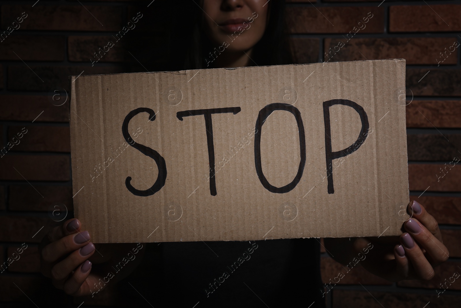 Photo of Young woman with sign STOP near brick wall, closeup. Domestic violence concept