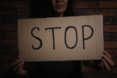 Photo of Young woman with sign STOP near brick wall, closeup. Domestic violence concept