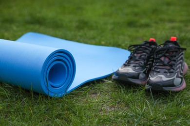 Photo of Blue karemat or fitness mat and sneakers on green grass outdoors