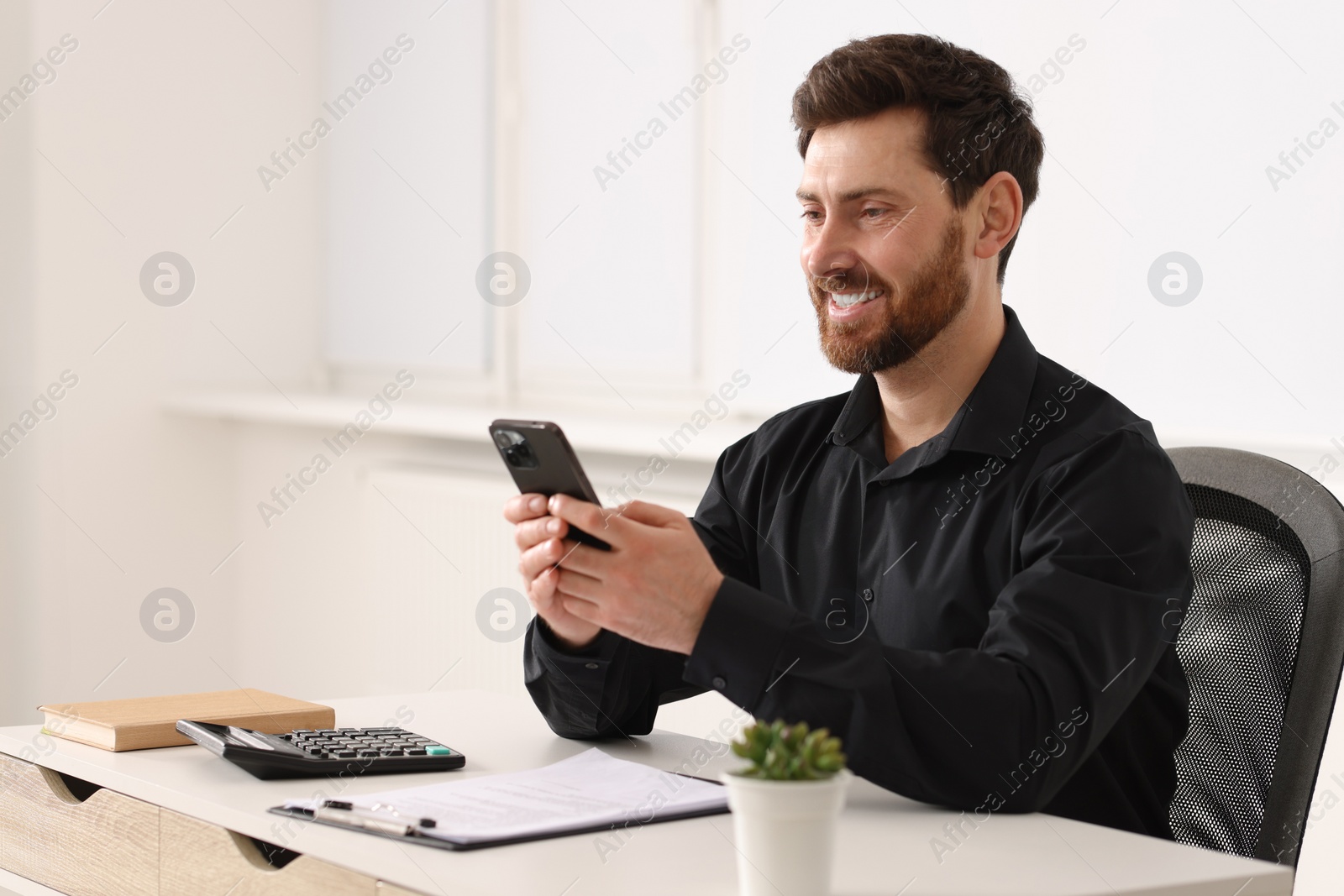 Photo of Smiling man using smartphone at table in office