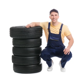 Male mechanic with car tires on white background