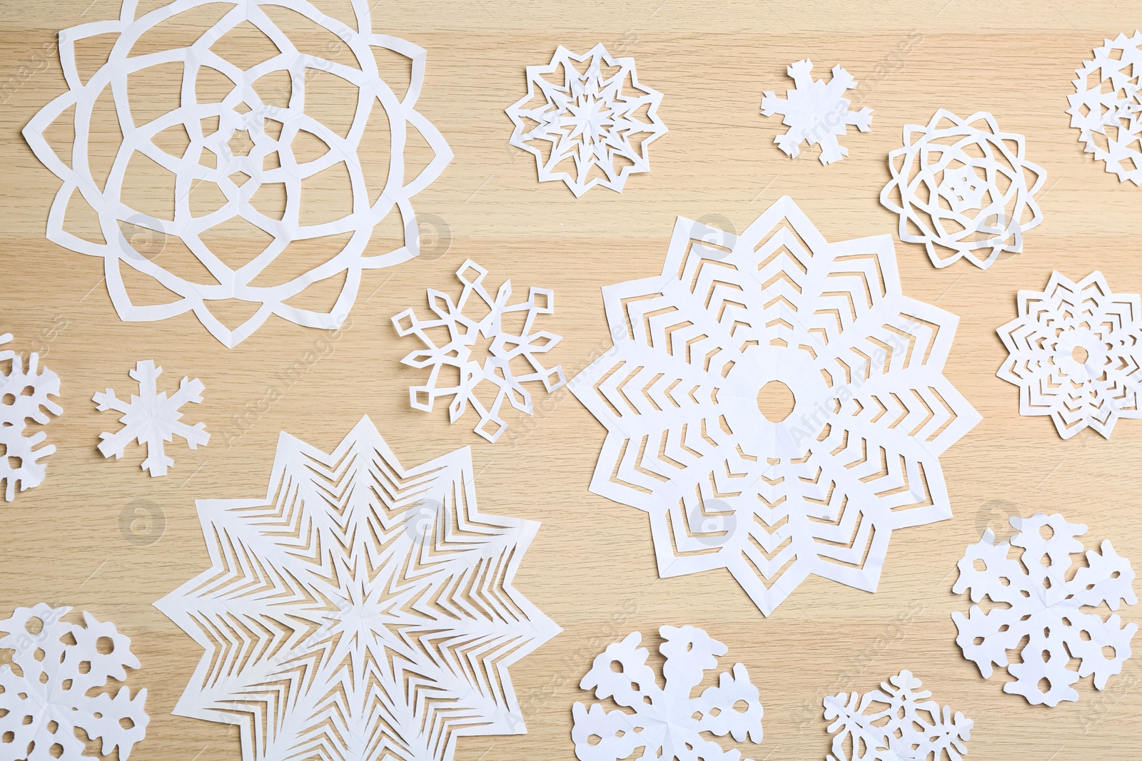 Photo of White paper snowflakes on wooden table, flat lay