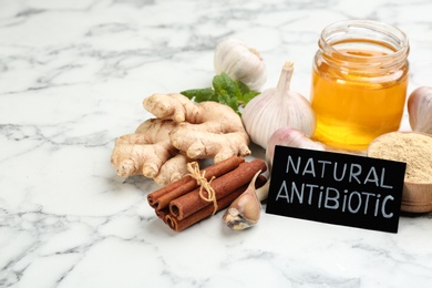 Photo of Different fresh products and card with phrase Natural Antibiotic on white marble table, space for text