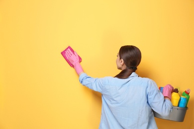 Woman with basin of detergents cleaning color wall