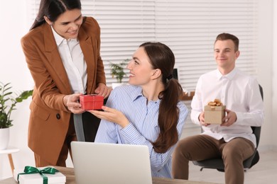 Photo of Woman presenting gift to her colleague in office