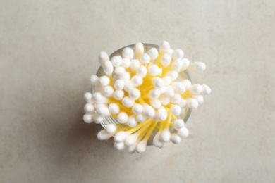 Glass with cotton swabs on grey background, top view