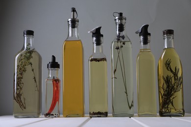 Photo of Bottles of different cooking oils on white wooden table against grey background