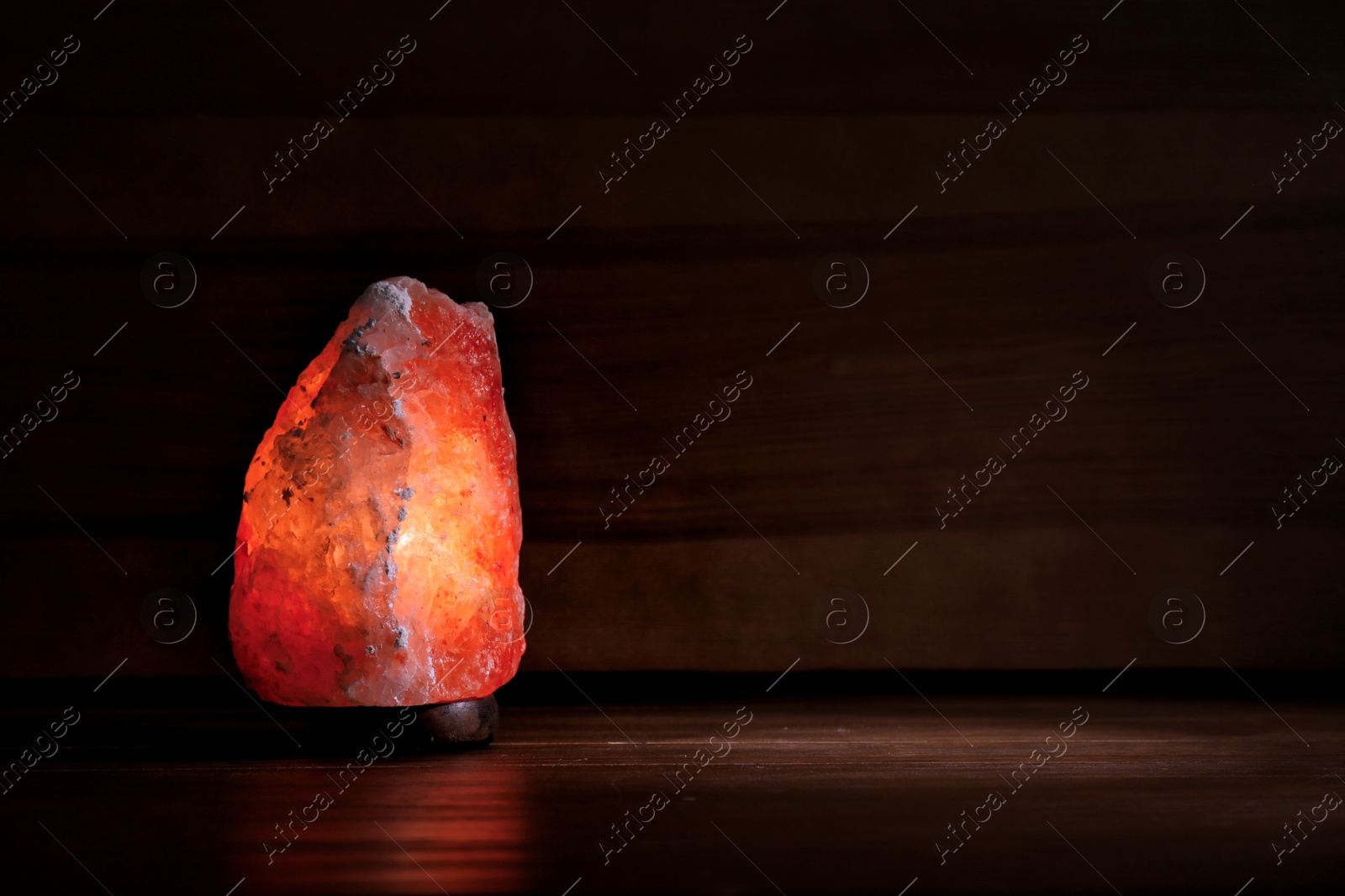 Photo of Himalayan salt lamp glowing on dark background with space for text