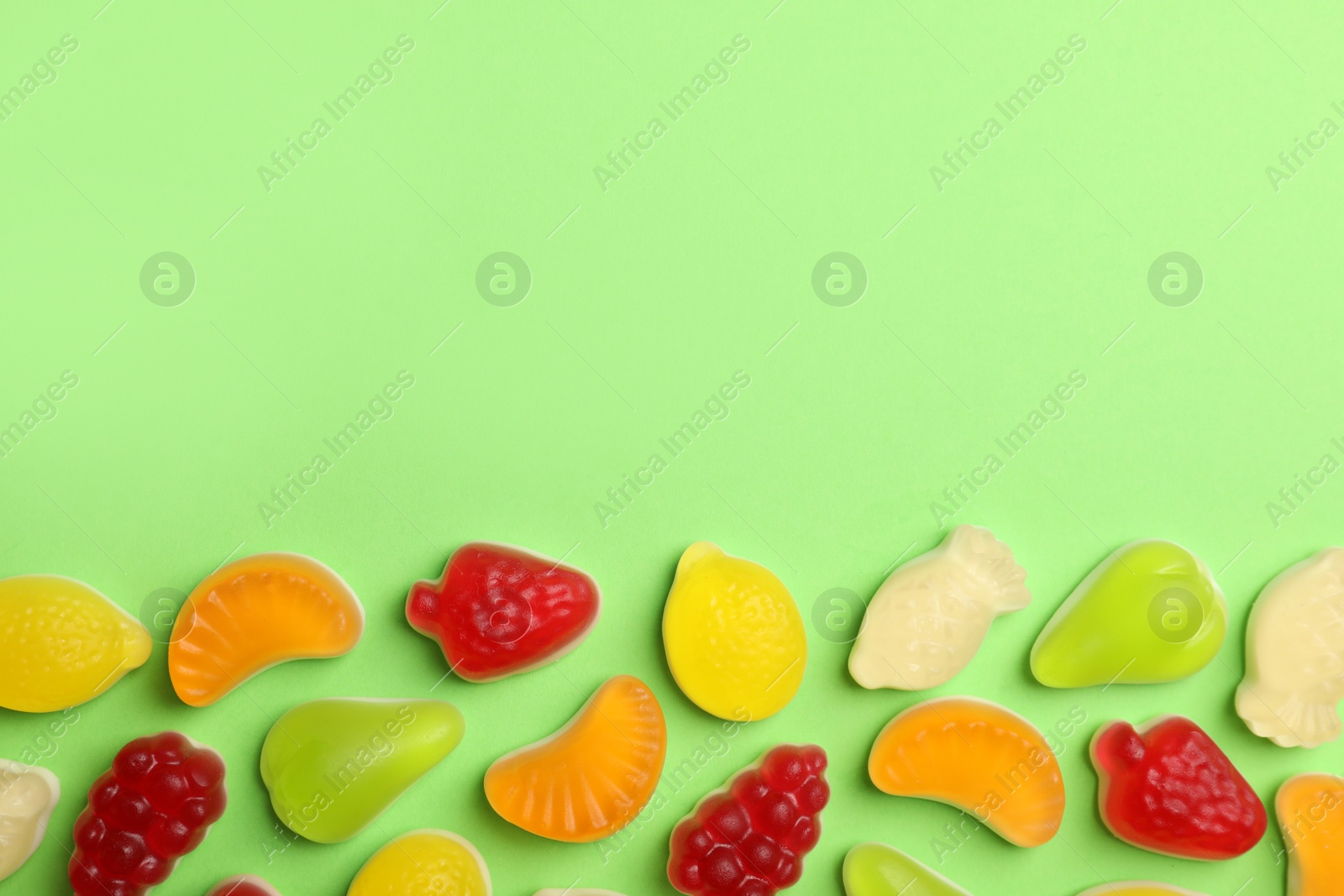 Photo of Delicious gummy fruit shaped candies on green background, flat lay. Space for text