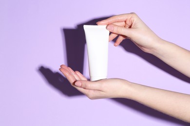 Woman holding tube of cream on violet background, closeup