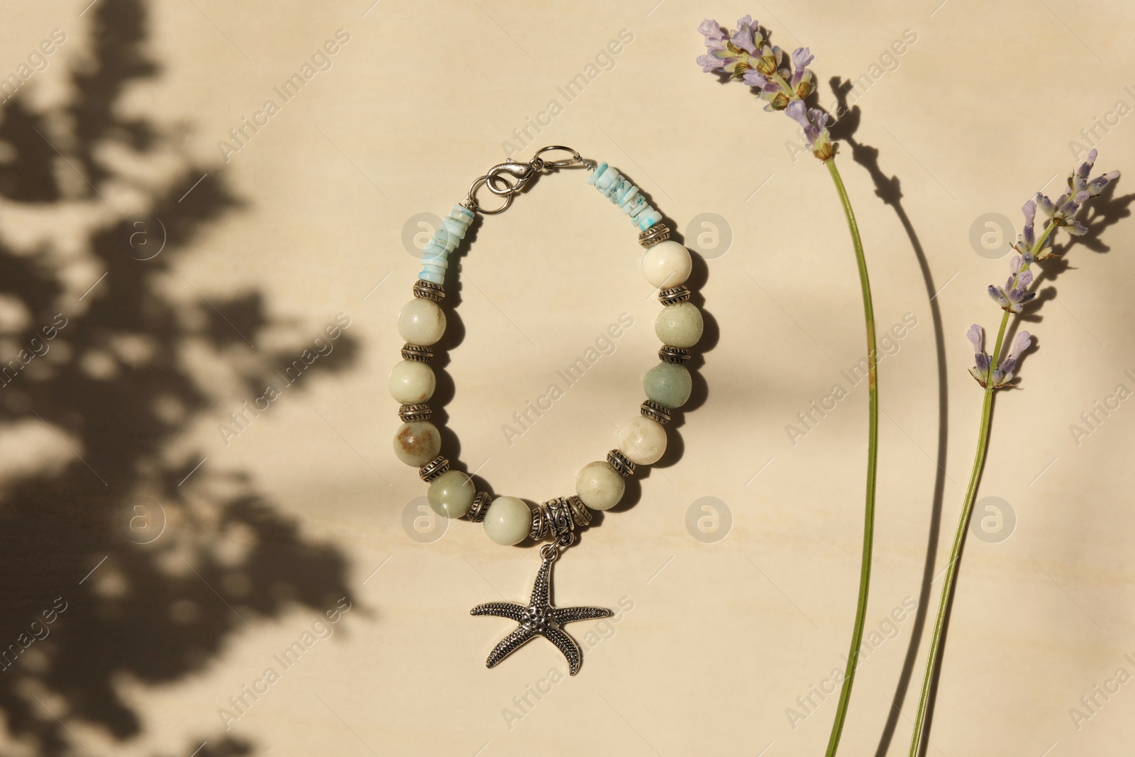 Photo of Beautiful bracelet with different gemstones and lavender flowers on beige background, flat lay