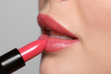 Photo of Young woman applying beautiful glossy lipstick on light background, closeup