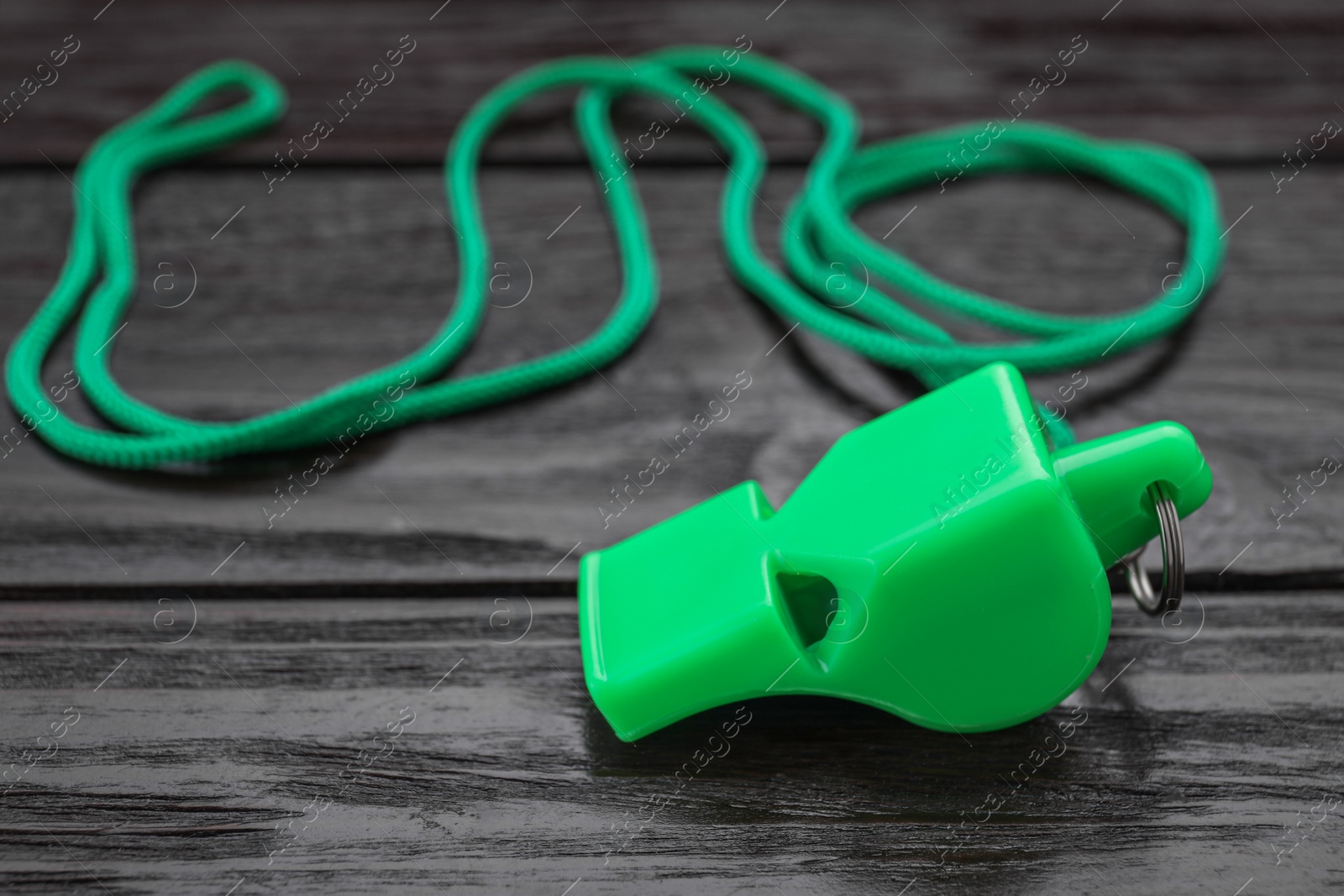 Photo of One green whistle with cord on wooden table, closeup. Space for text