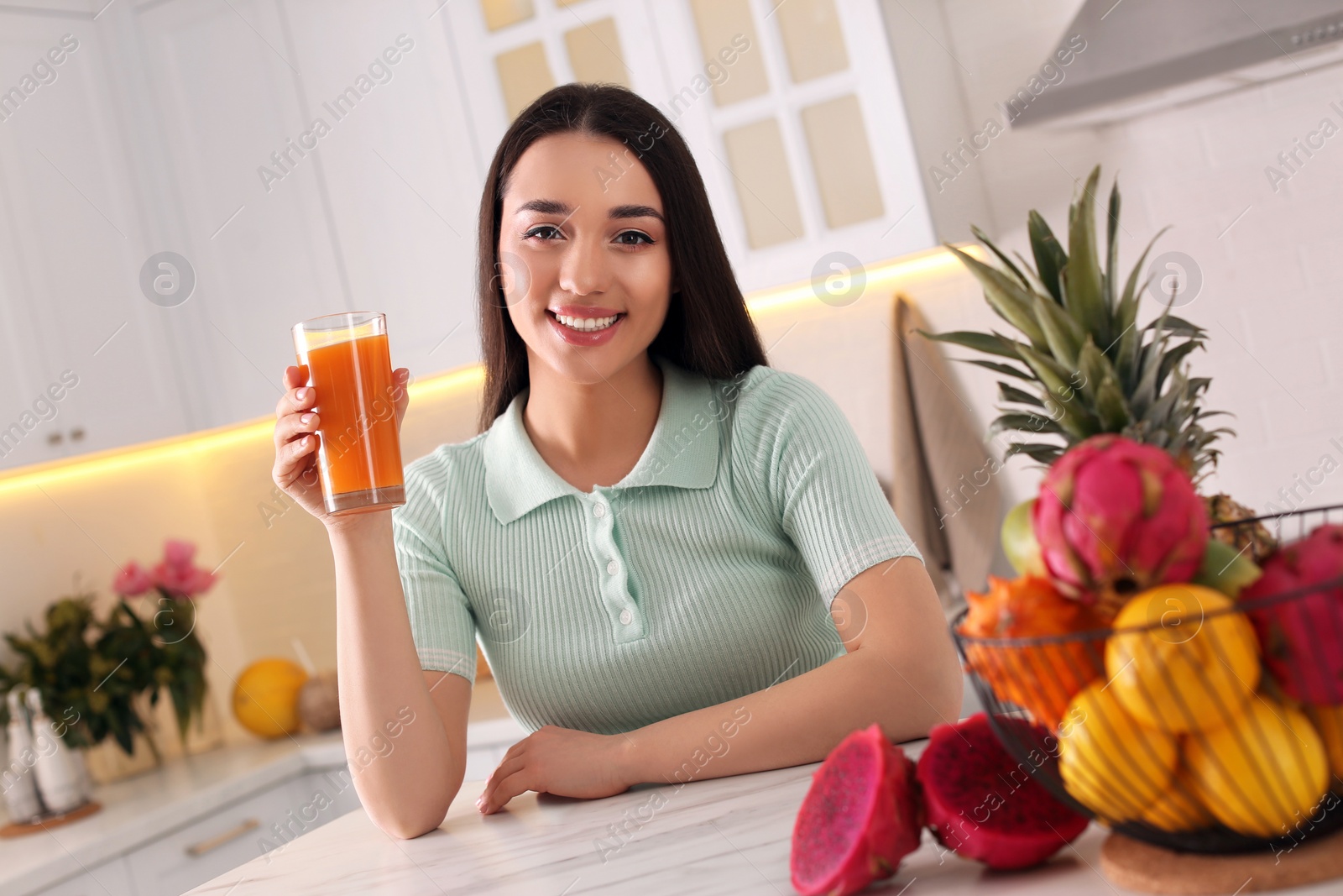 Photo of Young woman with glass of juice and exotic fruits in kitchen