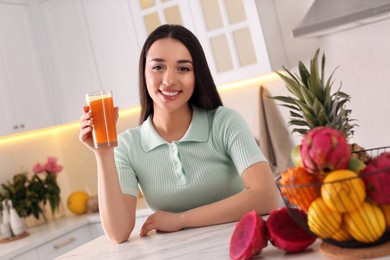 Young woman with glass of juice and exotic fruits in kitchen