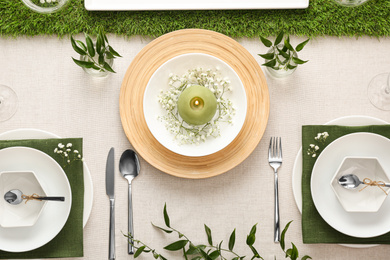 Elegant table setting with green plants on light cloth, flat lay