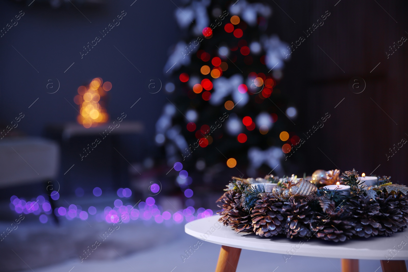 Photo of Beautiful wreath with pine cones on table and Christmas tree in dark room