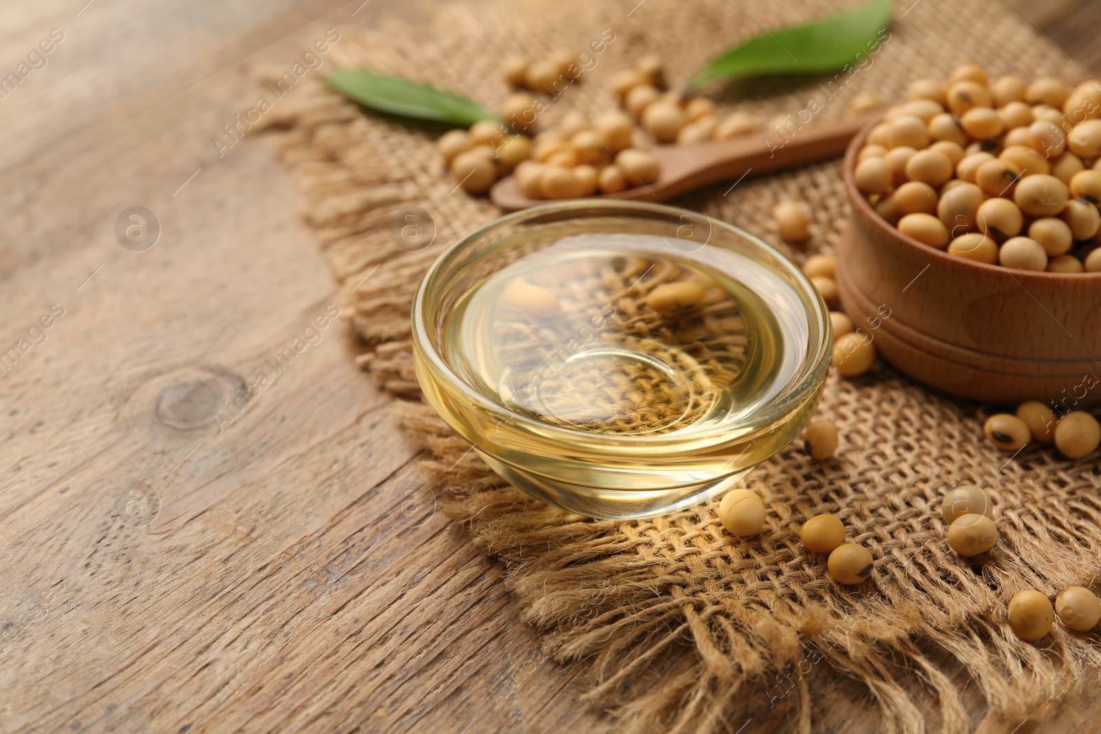 Photo of Glass bowl with oil and soybeans on wooden table, closeup