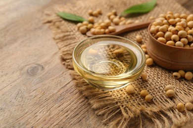 Glass bowl with oil and soybeans on wooden table, closeup