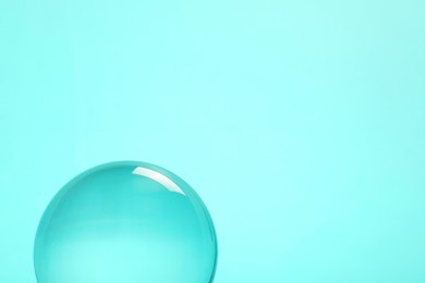 Photo of Transparent glass ball on turquoise background. Space for text