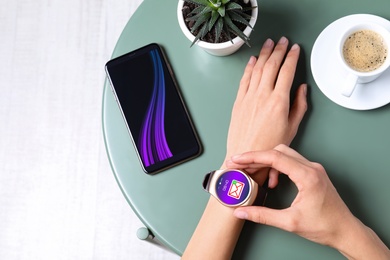 Image of Woman checking mail application in smart watch at table, top view