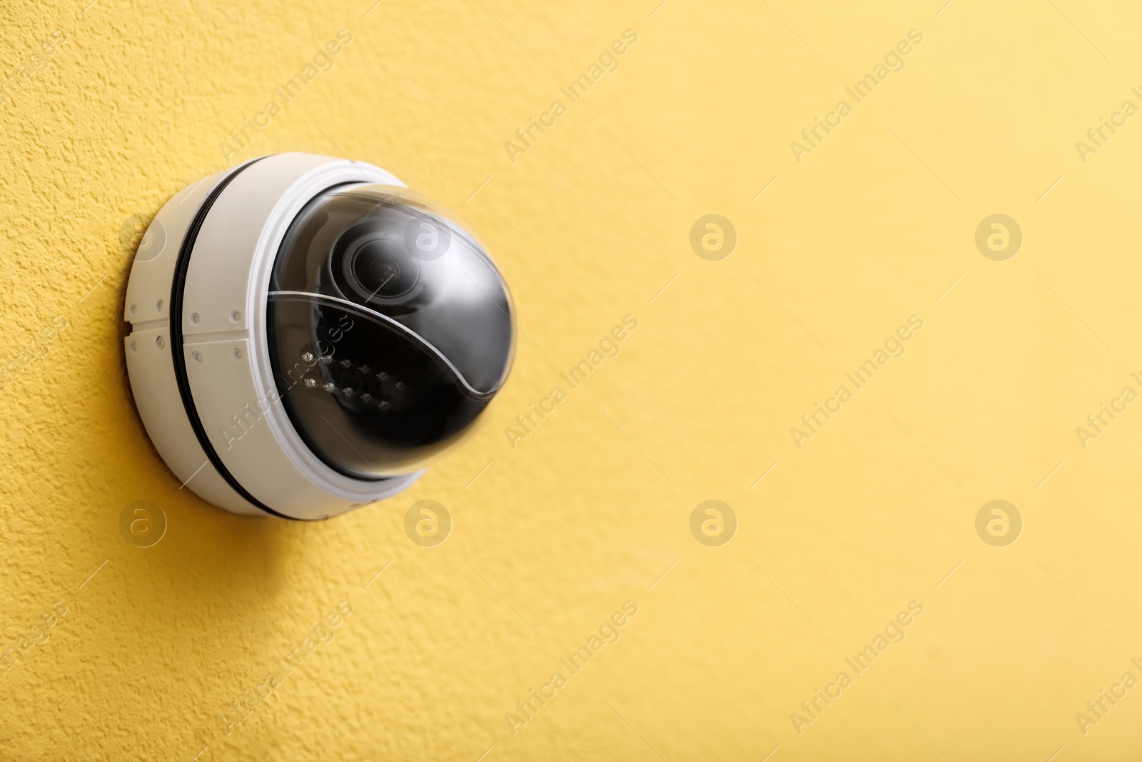 Photo of Modern CCTV security camera on yellow wall. Space for text