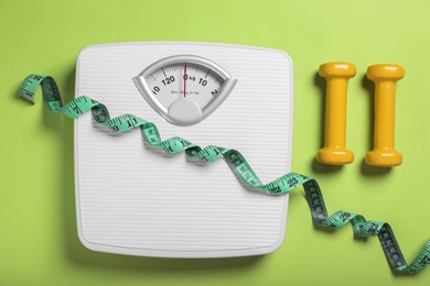 Weight loss concept. Scales, dumbbells and measuring tape on green background, flat lay