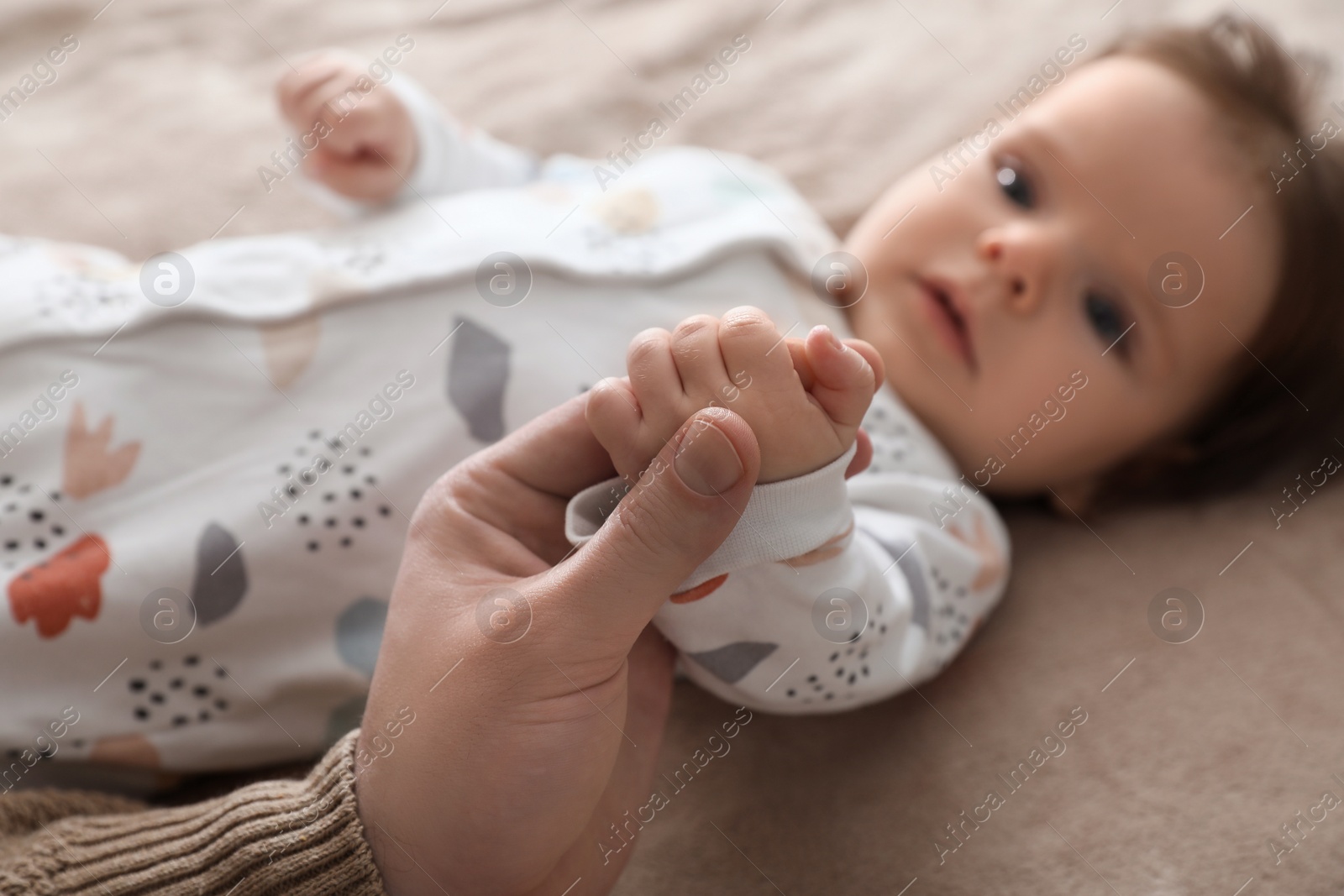 Photo of Father holding hands with his daughter on blanket, closeup