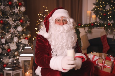 Photo of Santa Claus with glass of milk in room decorated for Christmas