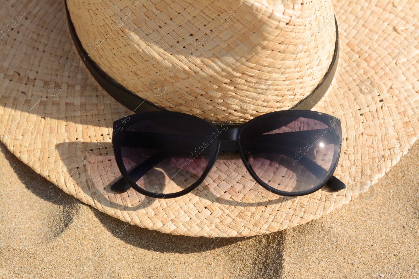 Photo of Hat with beautiful sunglasses on sand, closeup