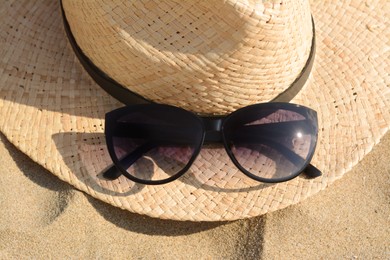 Photo of Hat with beautiful sunglasses on sand, closeup