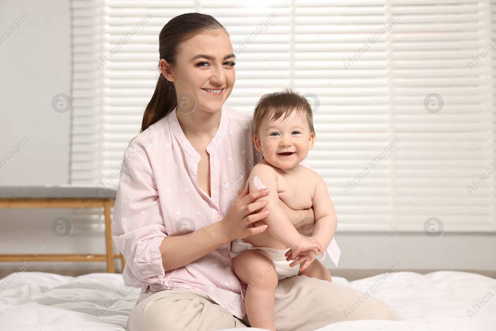 Photo of Happy mother applying body cream onto baby`s skin at home