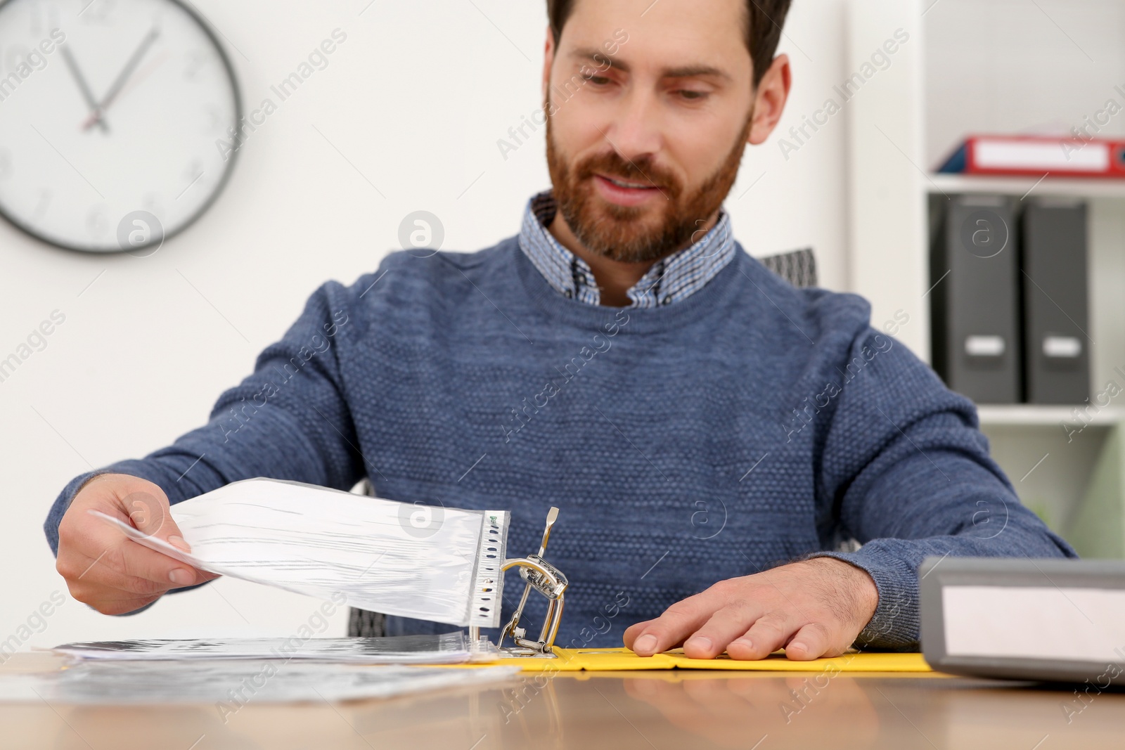 Photo of Businessman putting document into file folder at wooden table in office