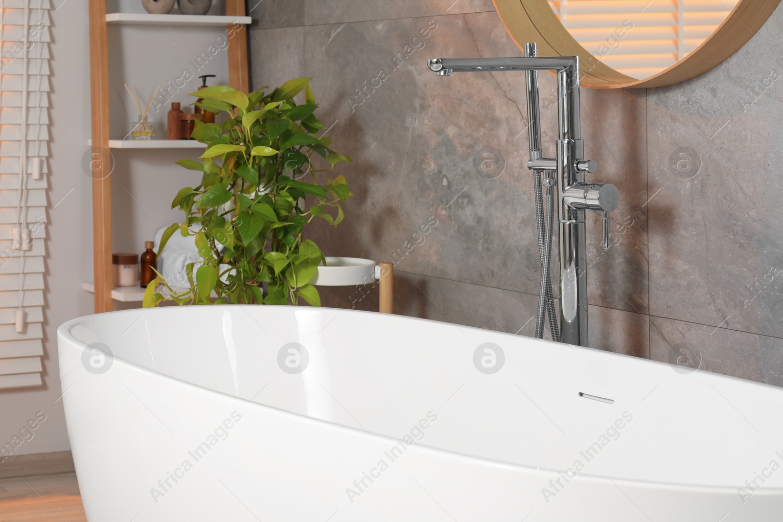 Photo of Spa day. Stylish bathroom interior with ceramic tub and green houseplant