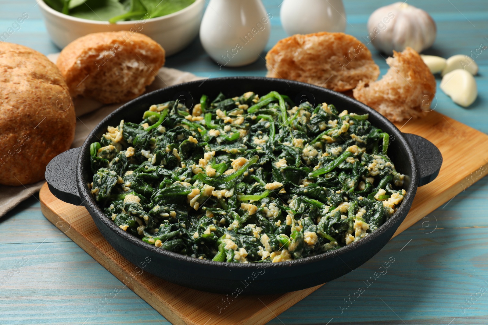 Photo of Tasty spinach dip with eggs in dish served on light blue wooden table, closeup