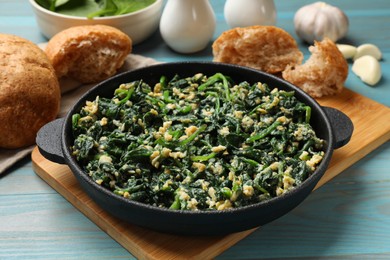 Tasty spinach dip with eggs in dish served on light blue wooden table, closeup