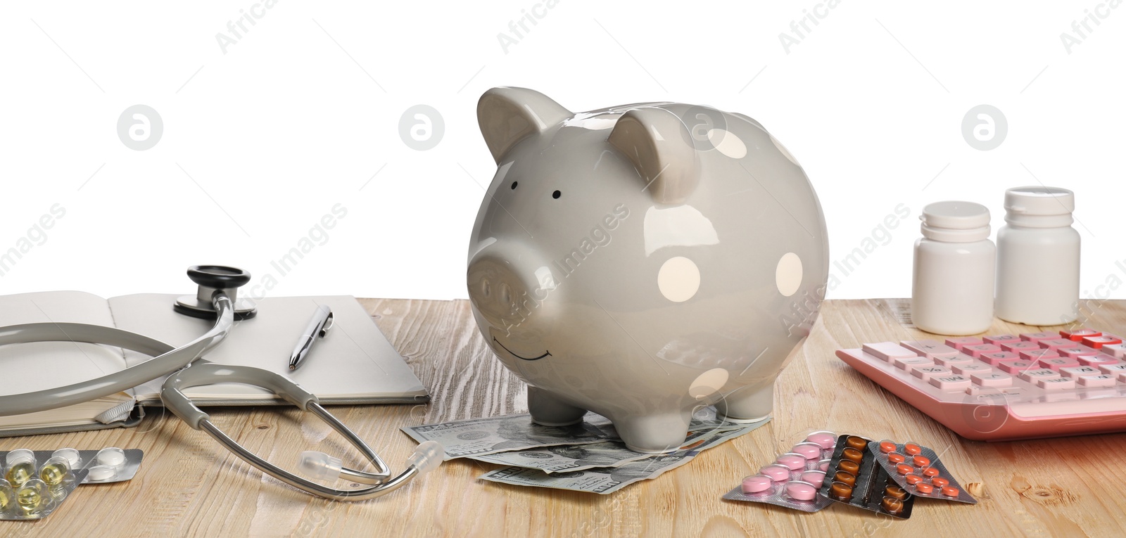 Photo of Piggy bank, stethoscope, calculator and pills on wooden table against white background. Medical insurance