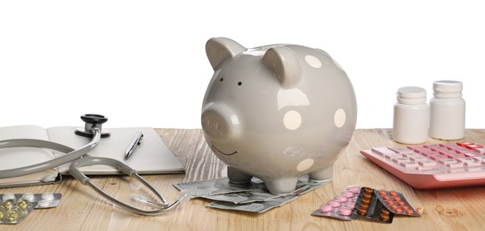 Piggy bank, stethoscope, calculator and pills on wooden table against white background. Medical insurance