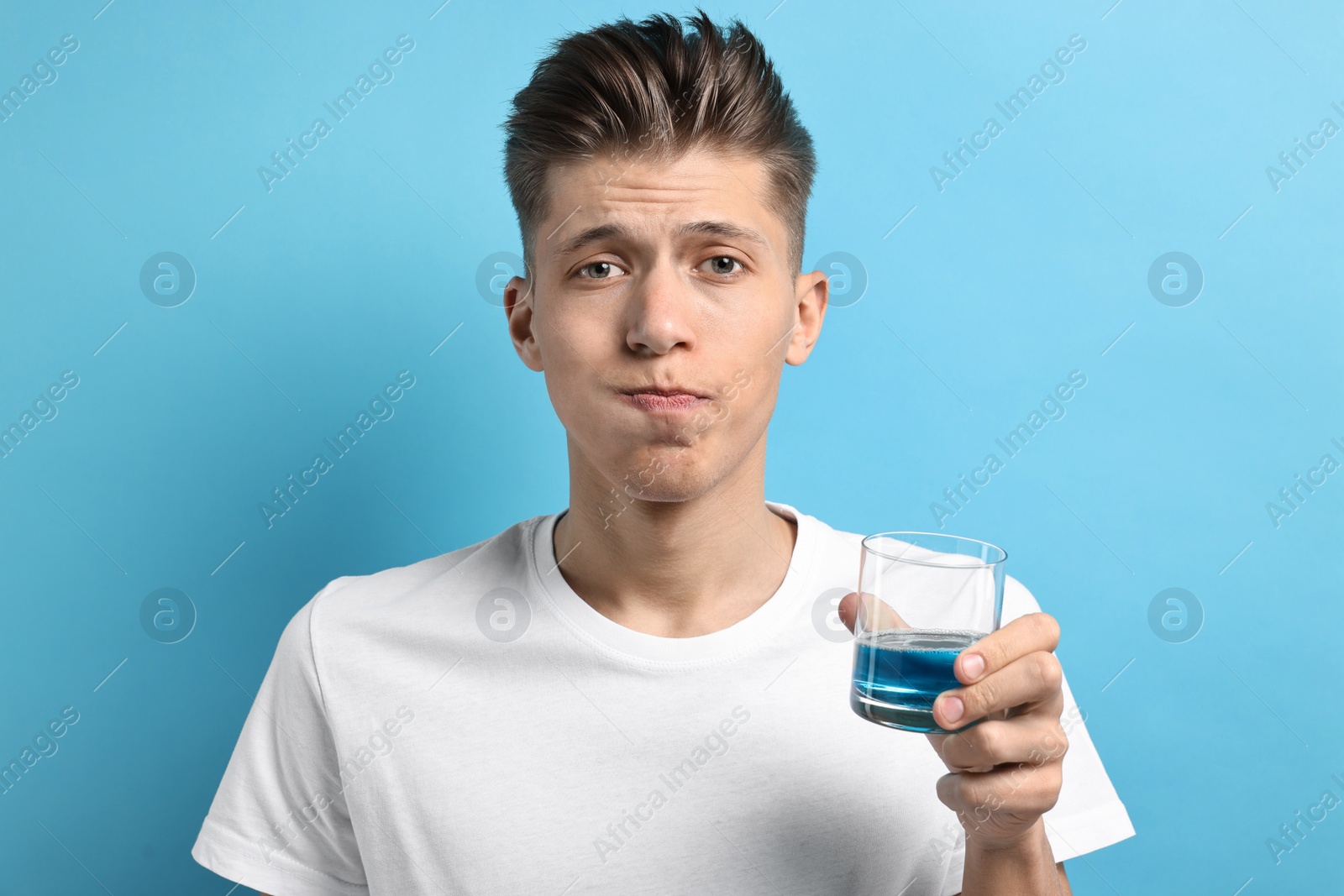 Photo of Young man using mouthwash on light blue background