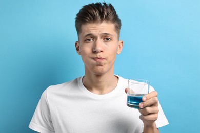 Young man using mouthwash on light blue background