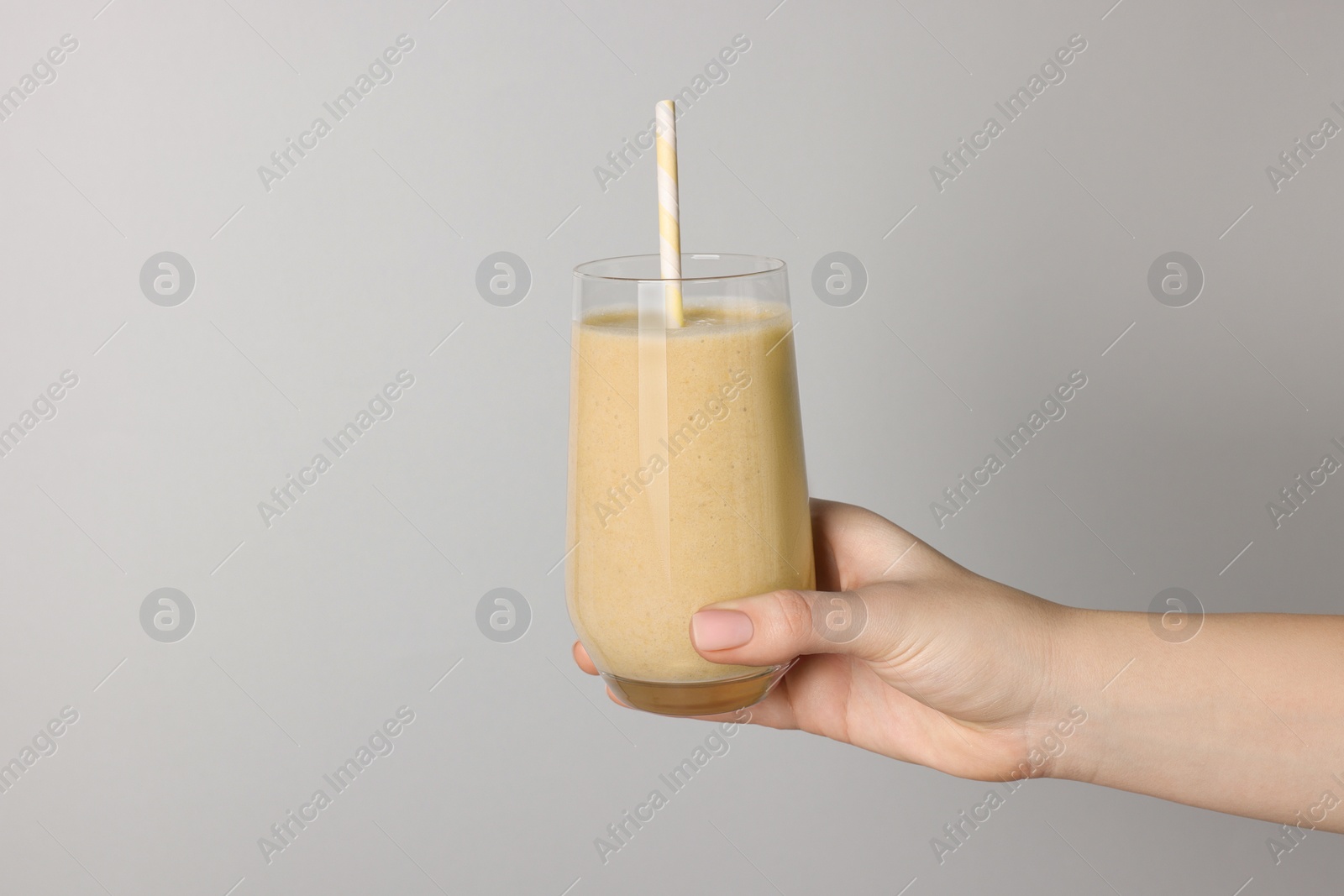 Photo of Woman holding glass of tasty smoothie on light grey background, closeup