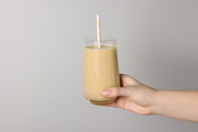 Photo of Woman holding glass of tasty smoothie on light grey background, closeup