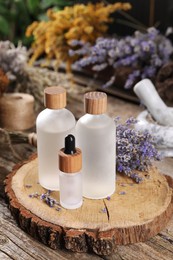 Bottles of essential oils and dry lavender flowers on wooden table, closeup. Medicinal herbs