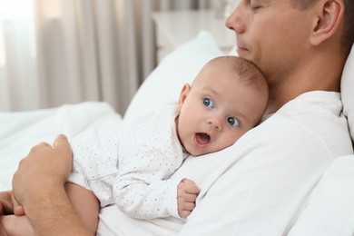 Father holding his cute baby on bed at home, closeup