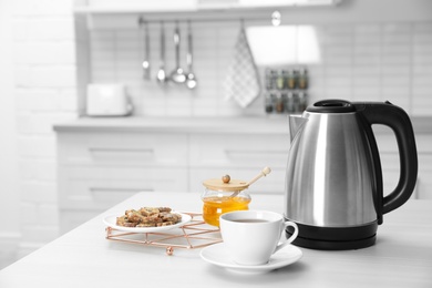 Modern electric kettle, cup of tea and cookies on wooden table in kitchen